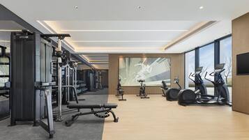A modern gym with various exercise equipment, large windows, and a spacious layout.