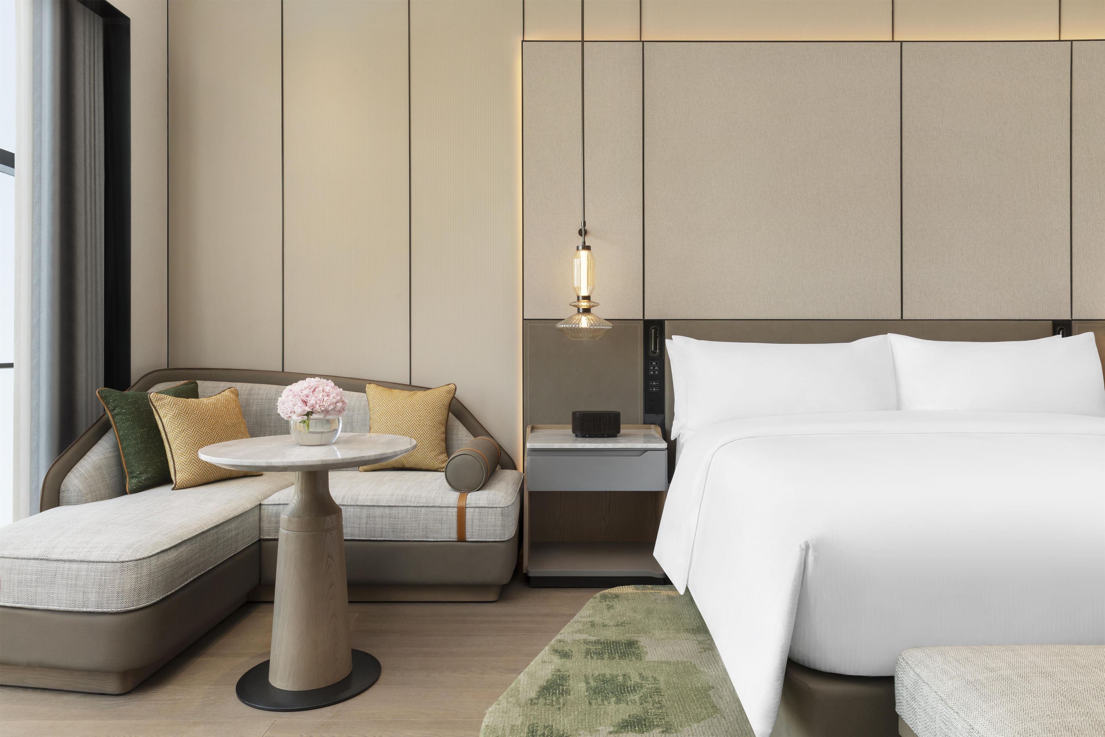 Une chambre d’hôtel moderne avec un canapé, une petite table ronde, une table de chevet et un lit.