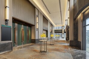 A modern hotel corridor with a patterned floor, vertical light fixtures, and a view of the city through large windows. - Doubletree by Hilton Zhengzhou Airport Aerotropol (Zhengzhou)