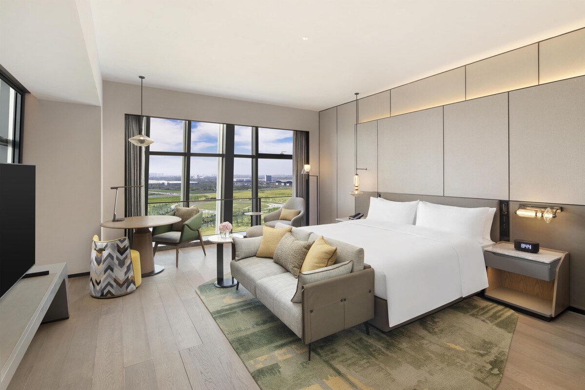 Une chambre d’hôtel moderne, dotée d’un grand lit, d’un canapé, d’un bureau et offrant une vue sur le paysage urbain.
