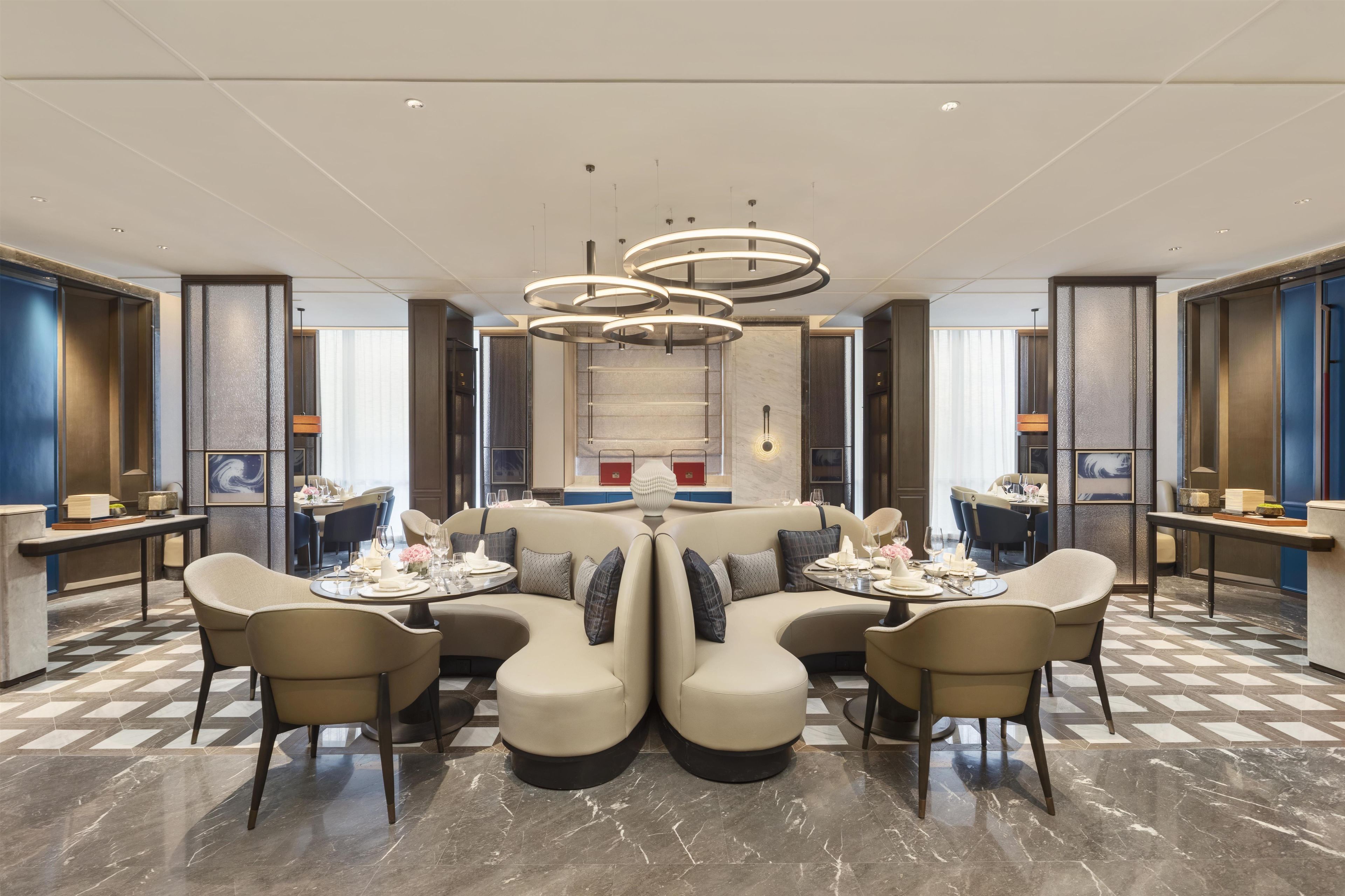 A modern hotel lobby with a central seating area, a staircase, and a view of the city.