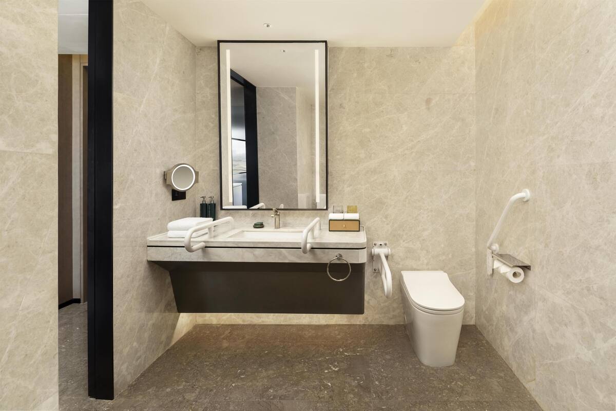 Une salle de bain moderne avec un grand miroir, un lavabo, des toilettes et un porte-serviettes.
