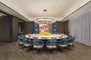Un comedor formal con una mesa redonda, sillas tapizadas en azul y una moderna lámpara de araña.