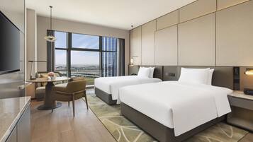 A hotel room with two beds, a dining area, a TV, and a large window with a city view.