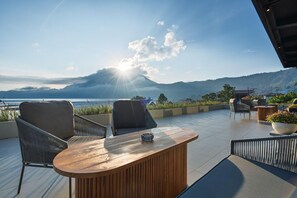 Una terrazza con tavolo e sedie di legno, vista su un lago e montagne.