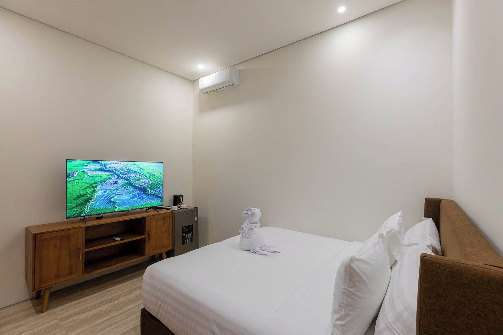 A hotel room with a bed, a TV on a wooden stand, a small cabinet, and a wall-mounted air conditioner.