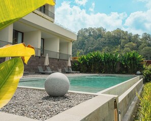 Un bâtiment moderne doté d’une piscine, entouré de plantes tropicales et surplombant un ciel dégagé.