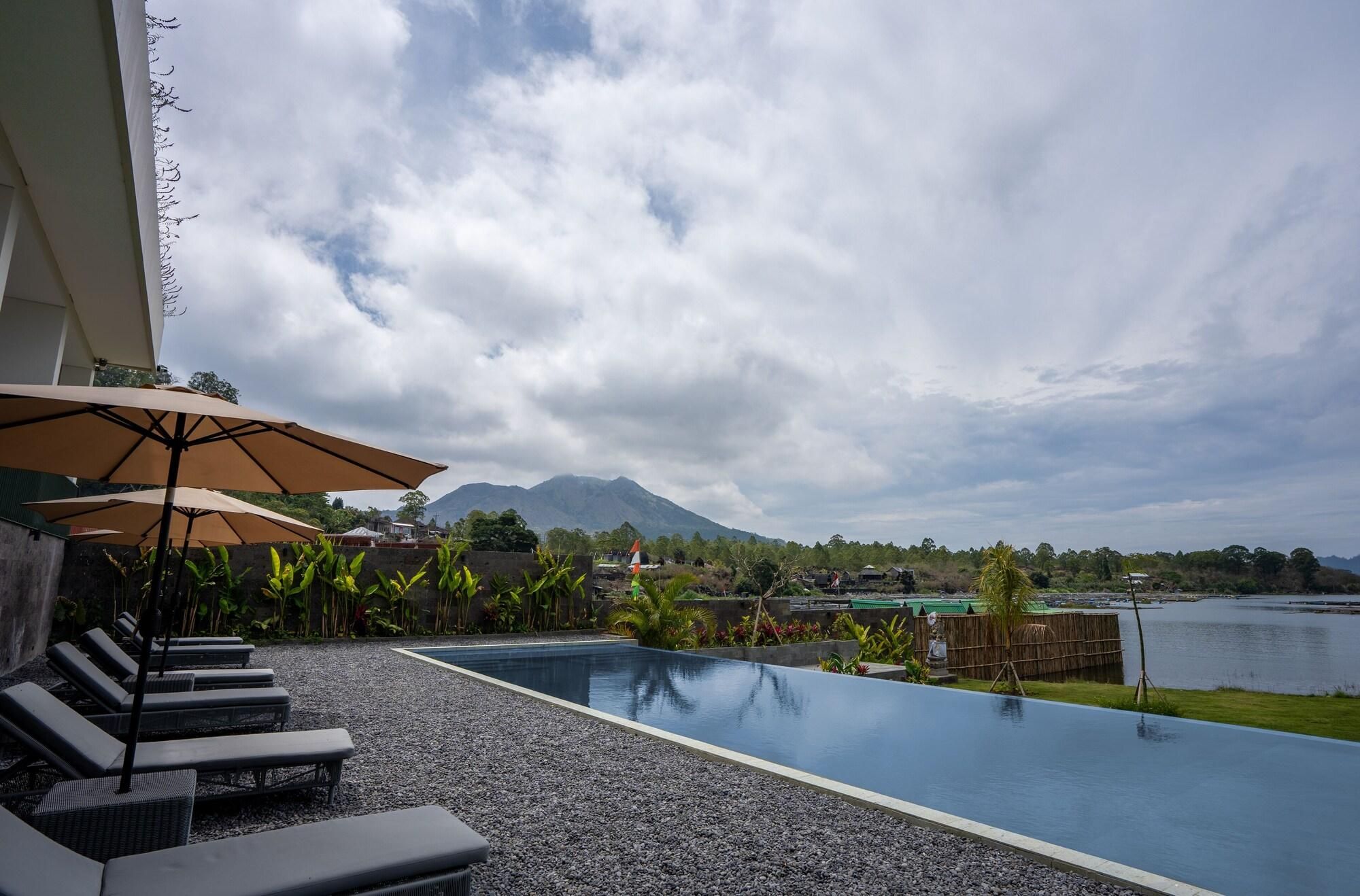 A pool area with lounge chairs and umbrellas, a mountain in the background, and a body of water.