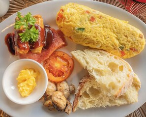 A plate with an omelette, bacon, a slice of tomato, scrambled eggs, and a piece of bread.