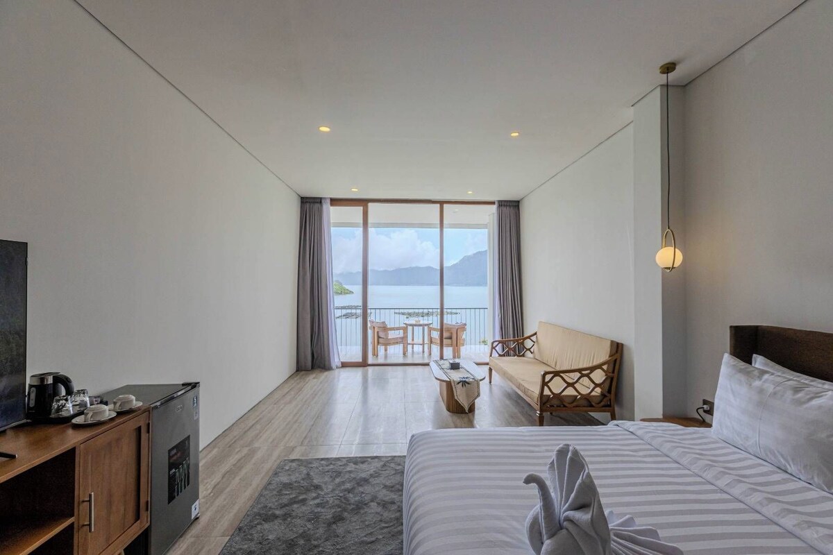Ein Hotelzimmer mit einem Bett, einer Couch, einem Esstisch mit Stühlen, einem Fernseher und Blick auf das Meer.