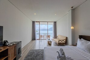 Ein Hotelzimmer mit einem Bett, einer Couch, einem Esstisch mit Stühlen, einem Fernseher und Blick auf das Meer.
