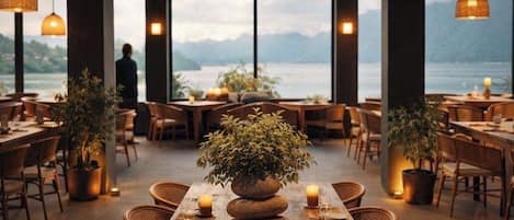 Un restaurant avec une table en bois dressée pour le repas, entourée de chaises, agrémentée de bougies et d’une plante en pot servant de centre de table.