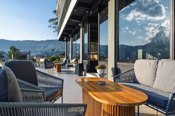 An outdoor seating area with wicker furniture and a wooden table, overlooking a mountainous landscape.