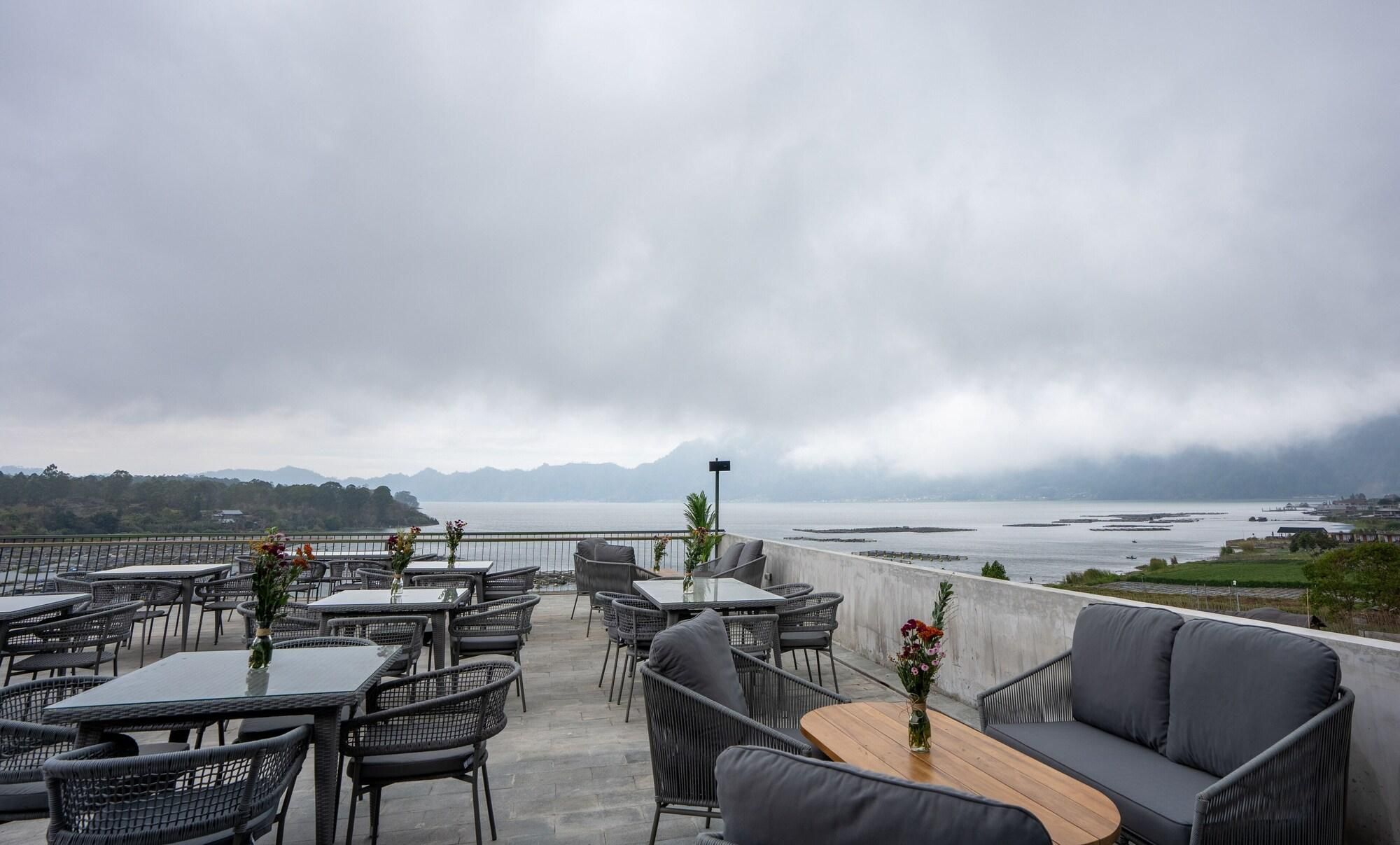 An outdoor seating area with tables and chairs, overlooking a body of water and distant mountains.