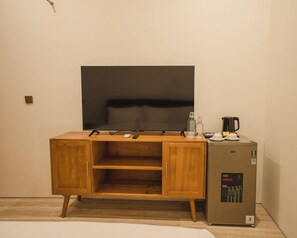 Une pièce comprenant un meuble en bois, un téléviseur à écran plat, un réfrigérateur de marque GEA et une machine à café.