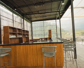 An indoor bar area with a wooden counter, bar stools, and shelves. - Tribhuwana Padma Resort (Kintamani)