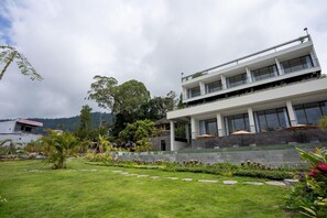 Un edificio moderno de dos pisos con techo plano, ventanas grandes y un balcón con mobiliario exterior.