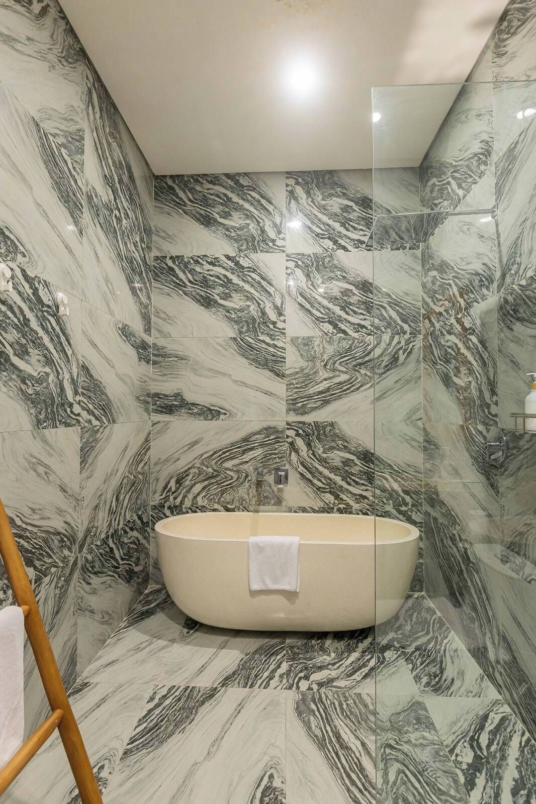Ein Badezimmer mit freistehender Badewanne, Wänden im Marmor-Look und einer Duschkabine aus Glas.