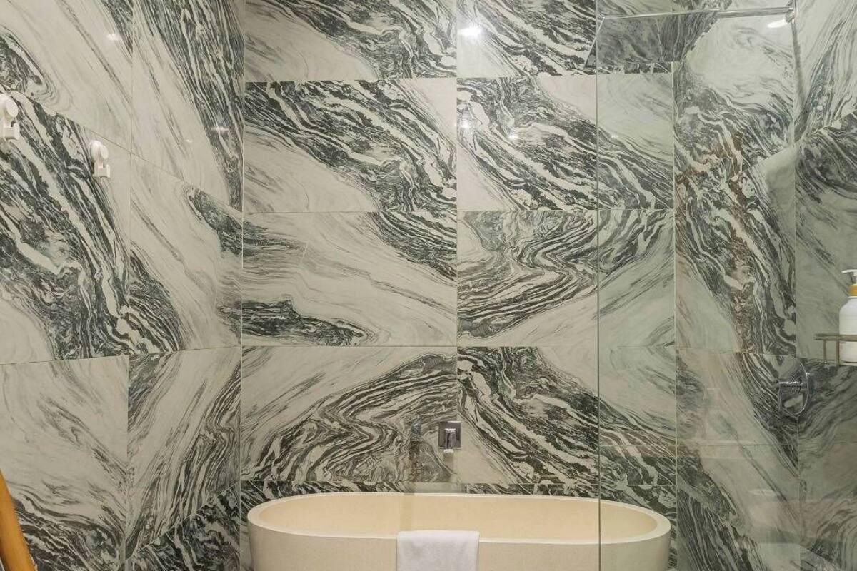 Une salle de bain dotée d’une baignoire îlot, de murs à motifs de marbre et d’une douche à parois de verre.
