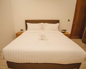 A neatly made bed with a wooden headboard, white bedding, and a pair of white slippers placed on the bed. - Tribhuwana Padma Resort (Kintamani)