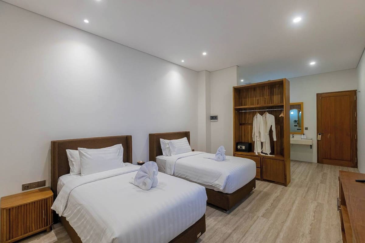 Hotellihuone, jossa on kaksi sänkyä, puinen vaatekaappi, peili ja puinen kaappi.
