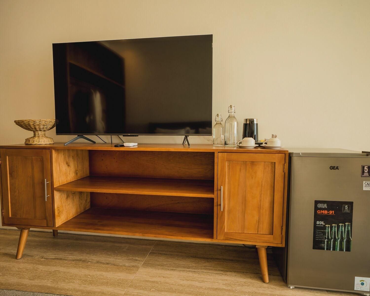 A wooden cabinet with a flat-screen TV, a small refrigerator, and a shelf with decorative items.