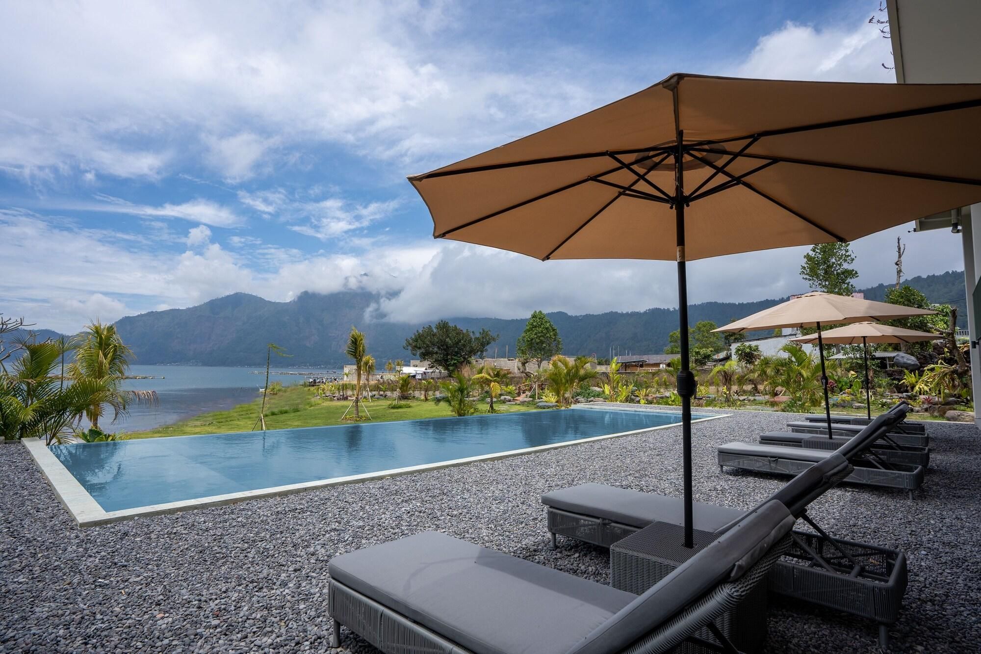 A pool area with lounge chairs and umbrellas, overlooking a body of water and mountains.