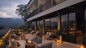 Un espace extérieur aménagé avec des canapés, des fauteuils et des tables, entouré de grandes fenêtres et de plantes en pot.