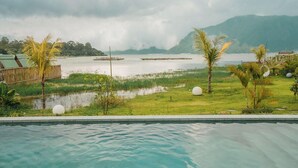 A swimming pool with a view of a calm lake, surrounded by greenery and a bamboo fence. - Tribhuwana Padma Resort (Kintamani)