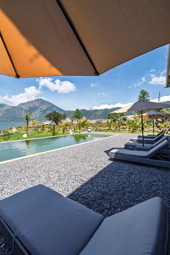A poolside area with lounge chairs, a pebble ground, and a view of mountains and a body of water. - Tribhuwana Padma Resort (Kintamani)