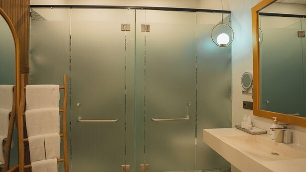 A modern bathroom with a glass shower enclosure, a wooden towel rack, and a large mirror. - Tribhuwana Padma Resort (Kintamani)