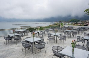 An outdoor terrace with tables and chairs, overlooking a body of water and a distant cityscape. - Tribhuwana Padma Resort (Kintamani)