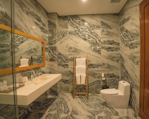 A bathroom with a marble-patterned wall, a wooden-framed mirror, a white sink, and a toilet. - Tribhuwana Padma Resort (Kintamani)