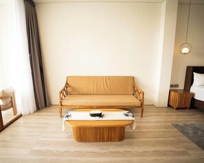 Una habitación de hotel moderna con sofá, una mesita de centro redonda de madera, una mesita auxiliar y una cama con cabecero.