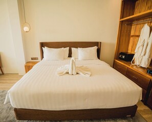 Una camera d'albergo con un letto grande, una testiera in legno, un comodino, un armadio e una lampada a sospensione.