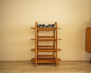 Un meuble à chaussures en bois, composé de plusieurs étagères, est placé contre un mur uni, et le sol est recouvert de carreaux.