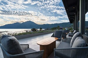 Una terraza con asientos al aire libre y vistas a un lago y montañas.