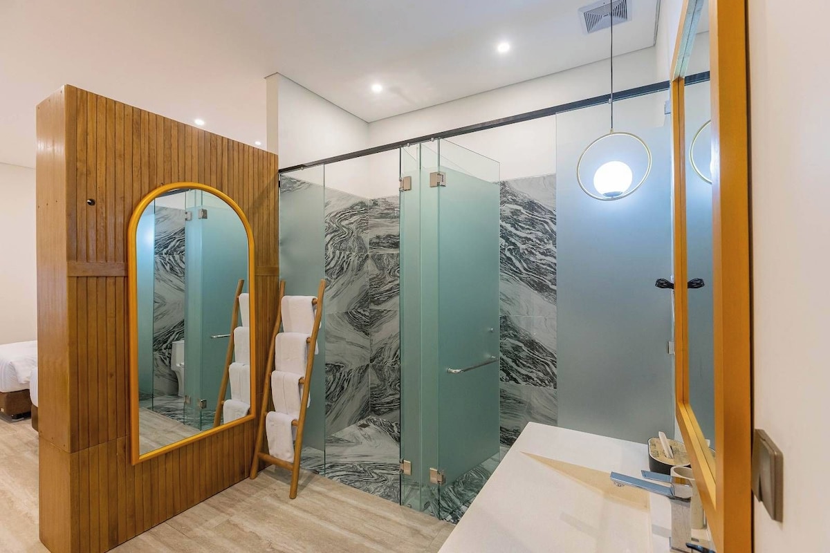 A modern bathroom with a wooden vanity, a large mirror, and a glass shower enclosure.