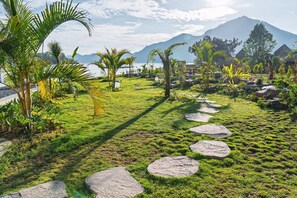 A landscaped garden with a stone pathway, palm trees, and a mountain in the background.