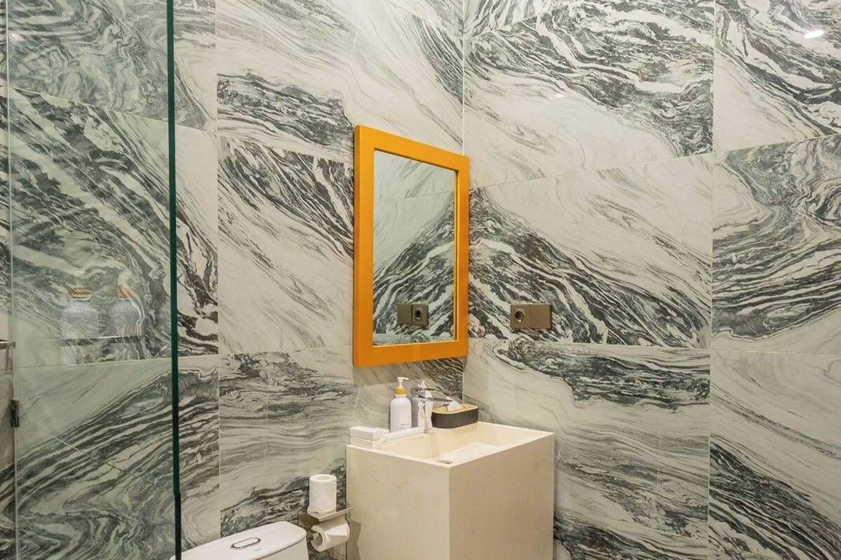A bathroom with a marble wall design, a glass shower enclosure, a white toilet, and a beige sink with a mirror above it.