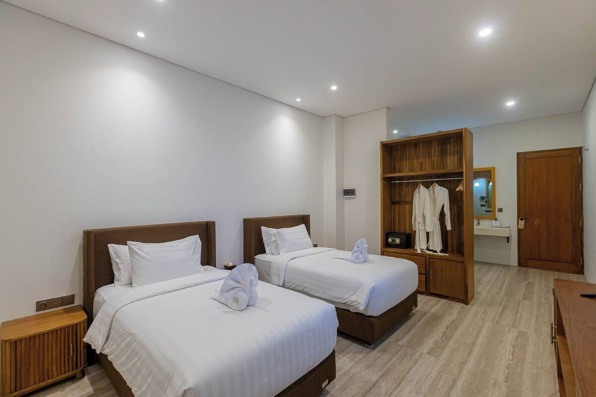 A hotel room with two beds, a wooden wardrobe, a mirror, and a wooden cabinet.