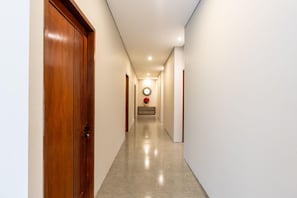Un couloir avec une porte en bois sur la gauche, un banc orné d’un vase de fleurs au centre, et un miroir rond accroché au mur.