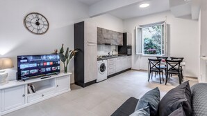 A modern kitchen with a built-in washer and dryer, a dining area with a table and chairs, and a large flat-screen TV mounted on a white cabinet. - PMT APT (Rome)