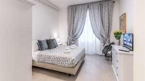 A neatly arranged bedroom with a bed, bedside table, and a desk with a computer. - PMT APT (Rome)