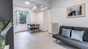 A modern living room with a dark sofa, a dining area with chairs, and a large window with a view of greenery. - PMT APT (Rome)