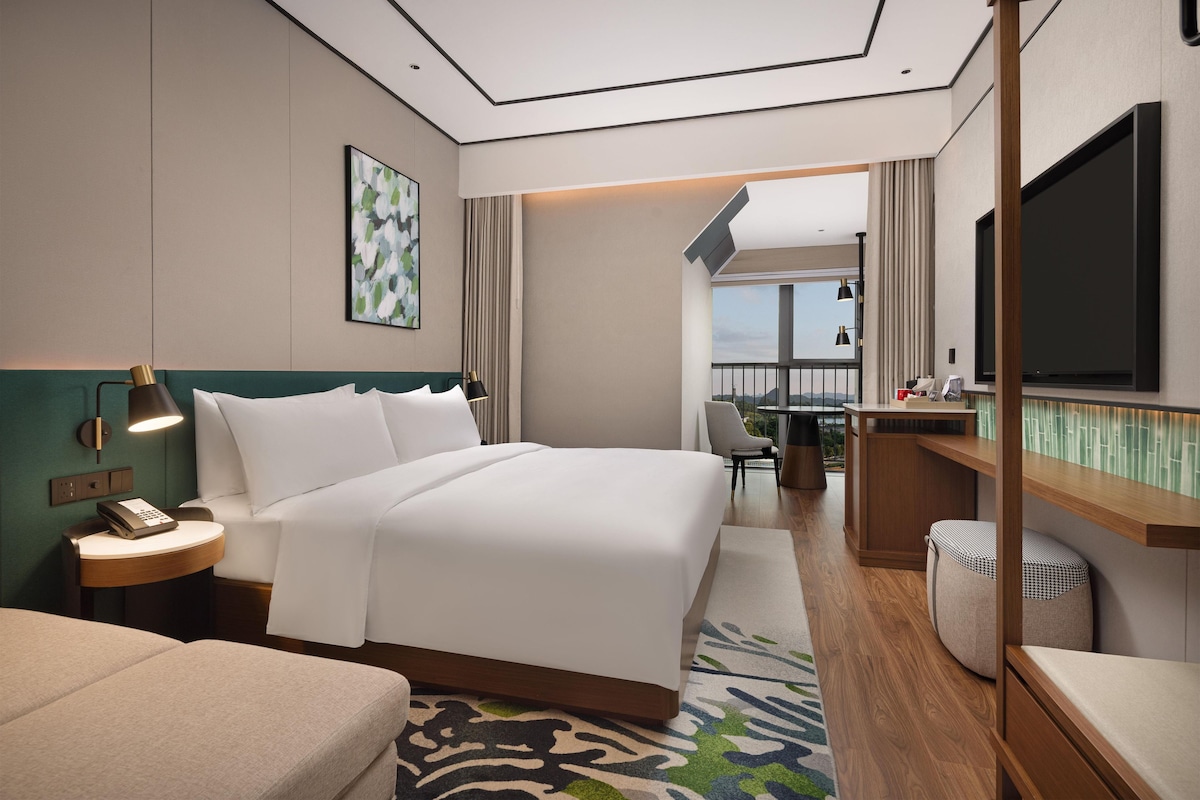 Une chambre d’hôtel moderne, dotée d’un grand lit, d’une table de chevet, d’une lampe et d’un téléviseur.