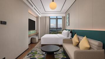 A hotel room with a bed, a sofa, a TV, and a large window with a city view.