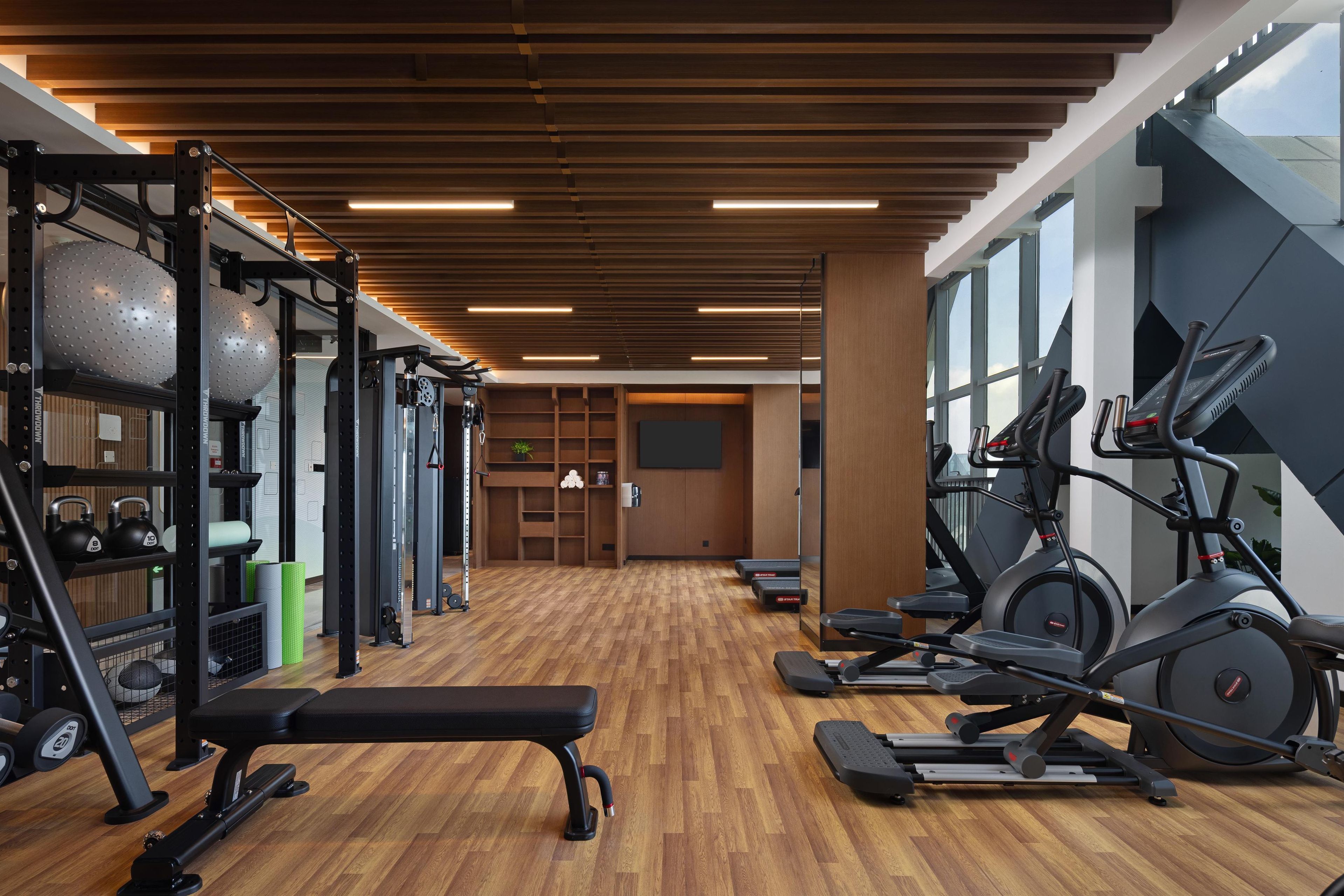 Une salle de sport équipée de matériel d’exercice, dotée d’un plancher en bois et de grandes fenêtres.