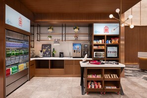 A modern kitchen with a refrigerator, microwave, and coffee machine. There are shelves with snacks and a small table with a fan. - Hilton Garden Inn Guiyang Gui'an New Area (Guiyang)