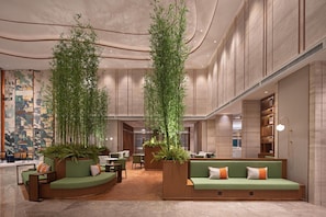 Eine großzügige Lobby mit einer gebogenen, grünen Couch, Holzmöbeln und hohen Bambuspflanzen.